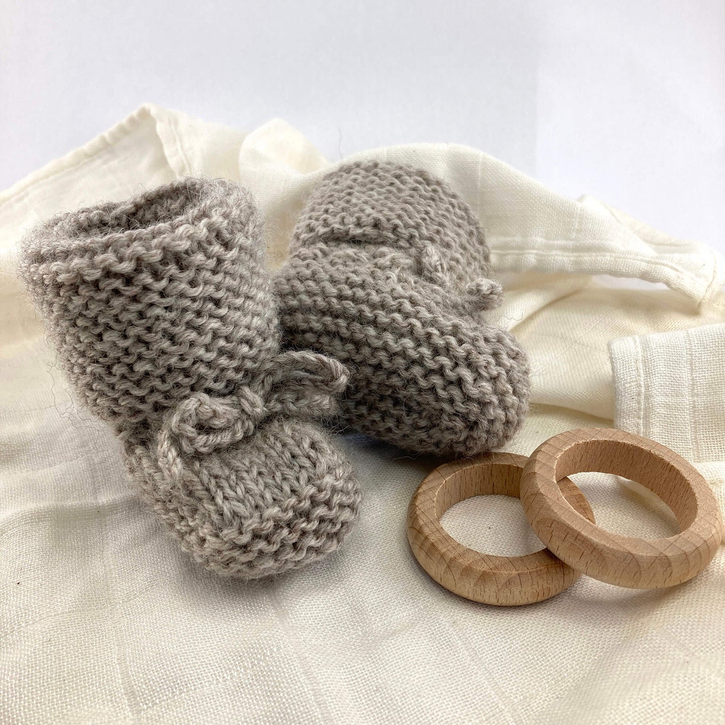 a baby knitting pattern for booties. the baby booties ate styled on a muslin with the underside of one showing the stitch detail