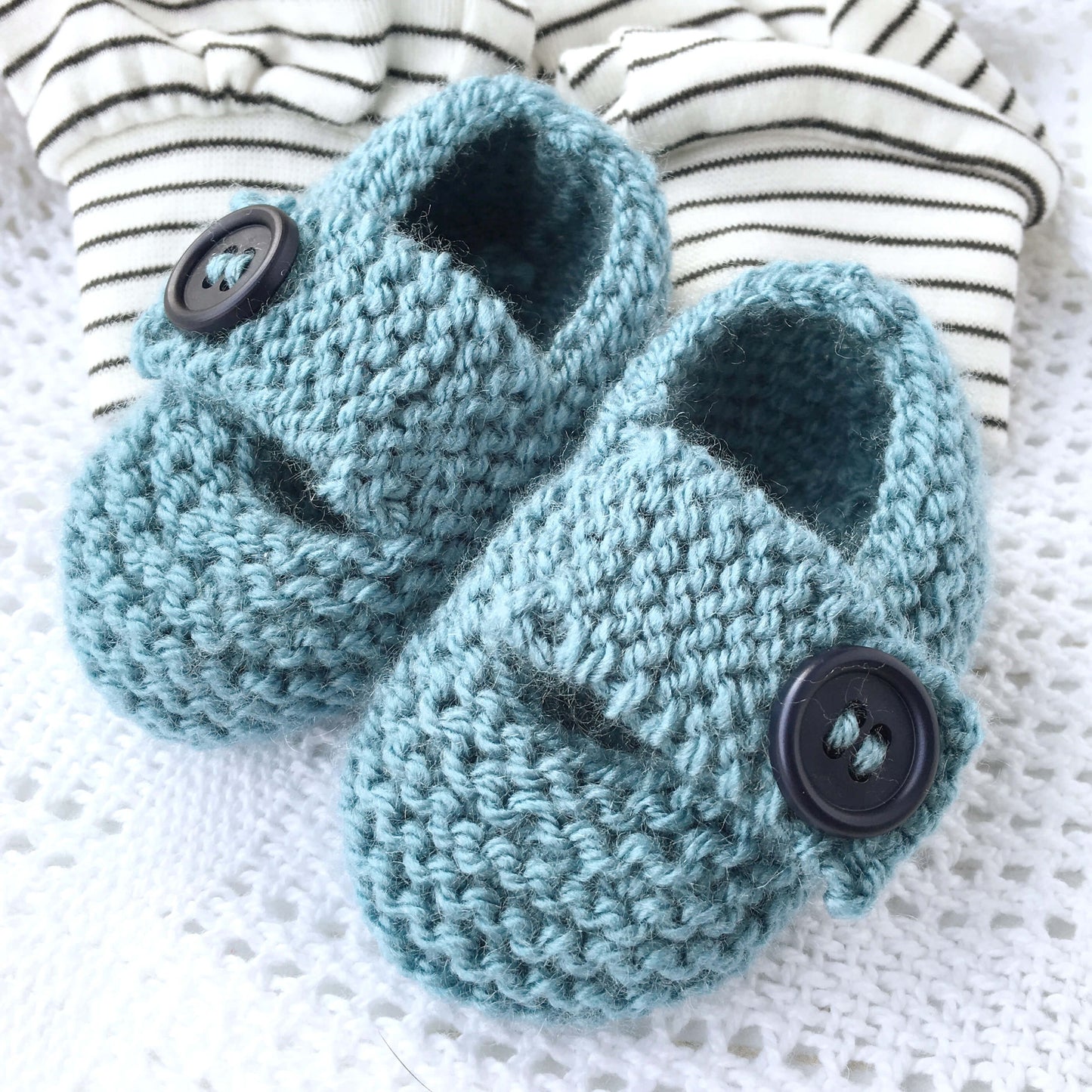a baby shoes knitting pattern. samples are knit in blue yarn with navy buttons