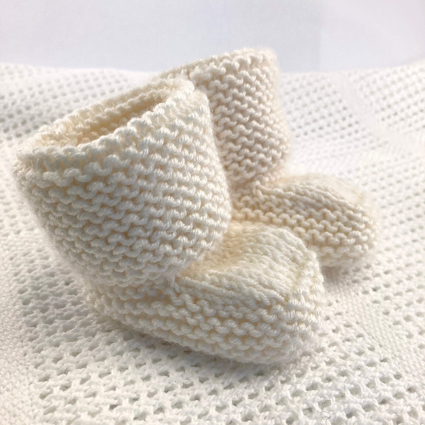 a beginner knitting pattern for baby booties. sample knitted in white yarn and styled on a baby blanket