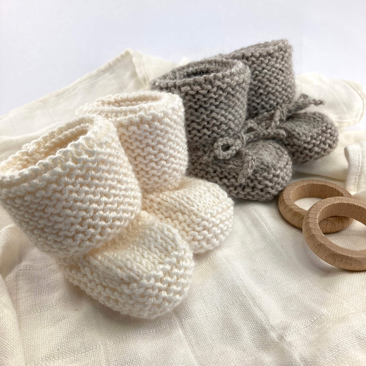 a baby booties pdf knitting pattern for two styles of booties. one is shown in grey with knitted ties, the other in white yarn without ties