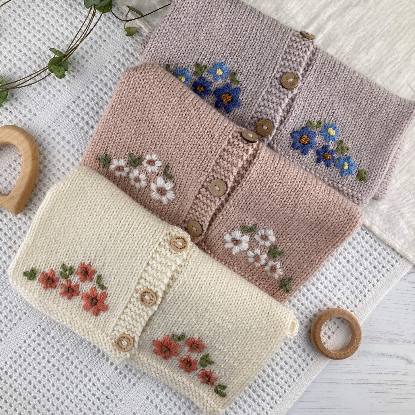 Knitting pattern for baby cardigan with floral pattern. 3 samples shown folded on a baby blanket