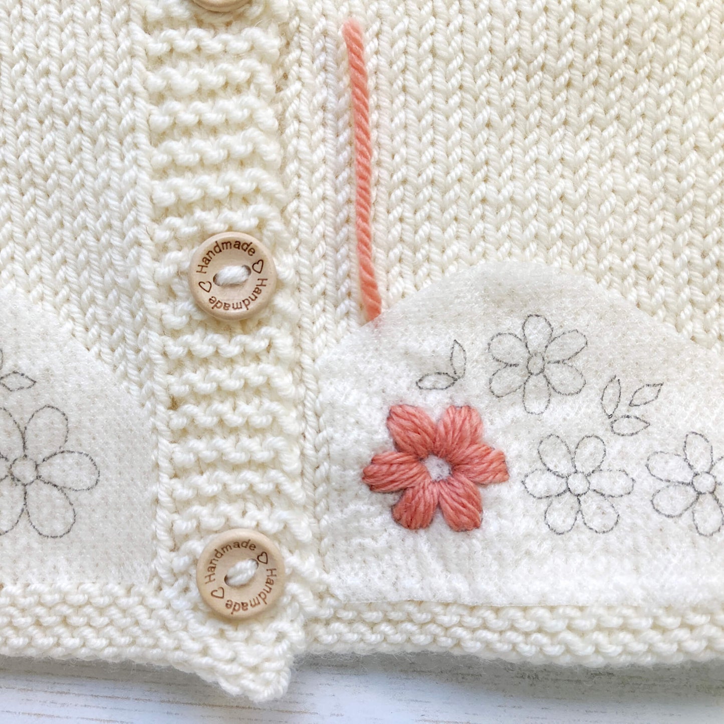 Close-up of flower embroidery process for a baby cardigan knitting pattern.