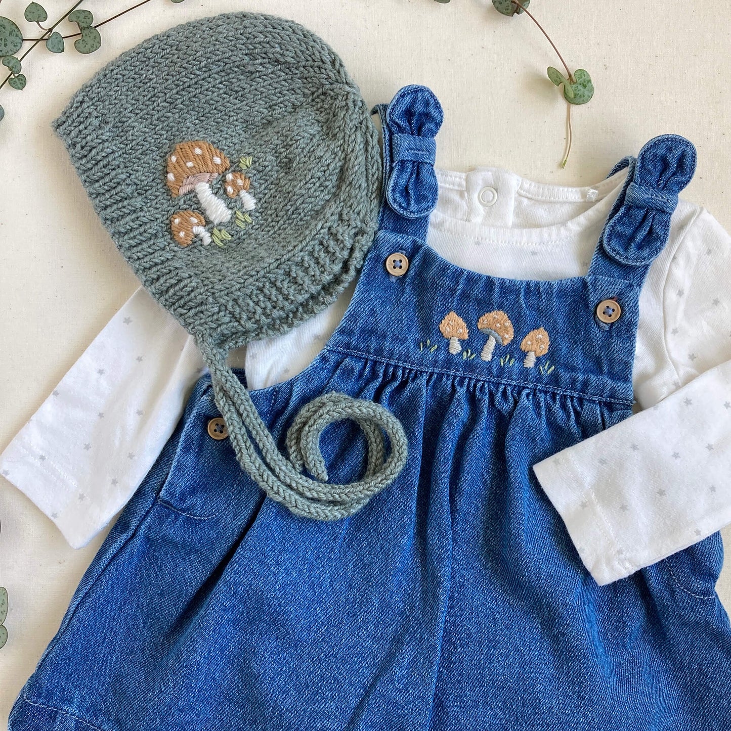 a hand embroidery pattern for baby clothes. embroidered toadstools are shown on a bonnet and pinafore dress