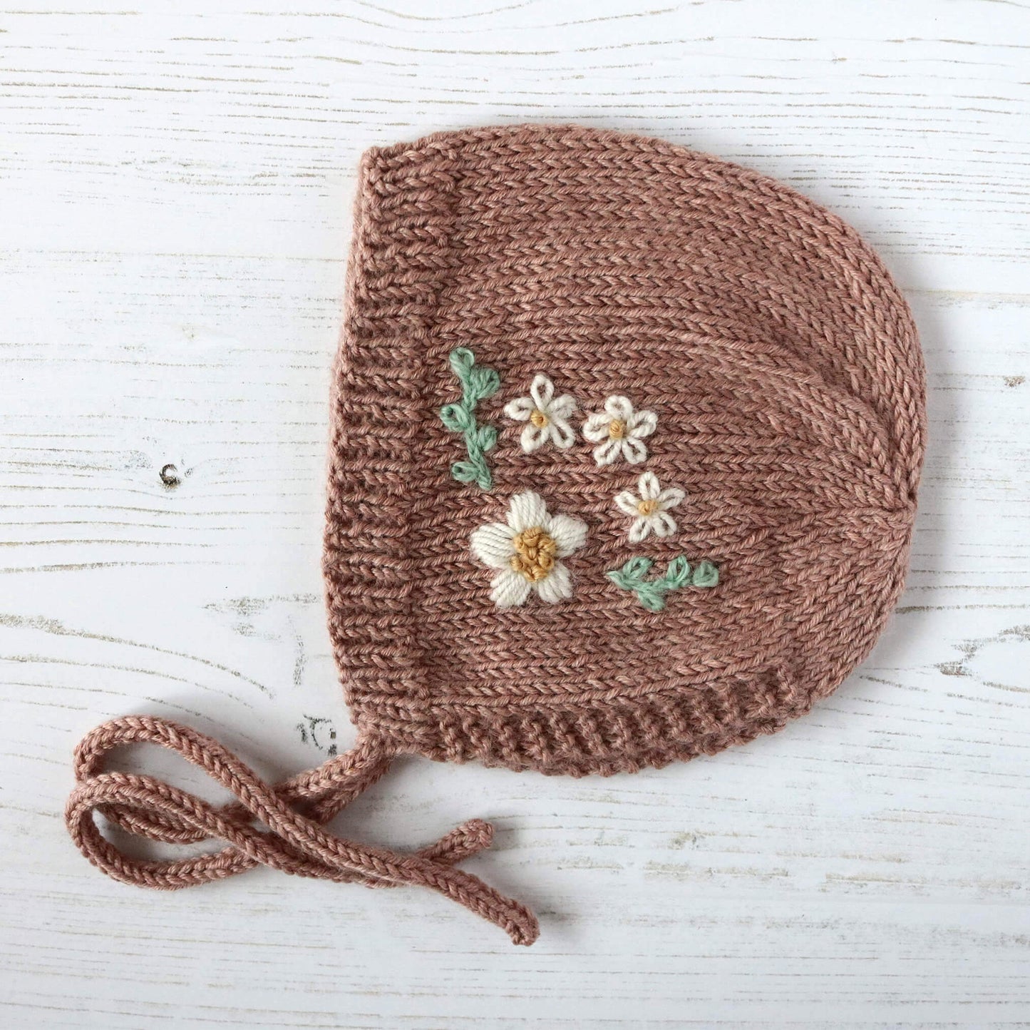 a knitting pattern for a baby bonnet with floral embroidery