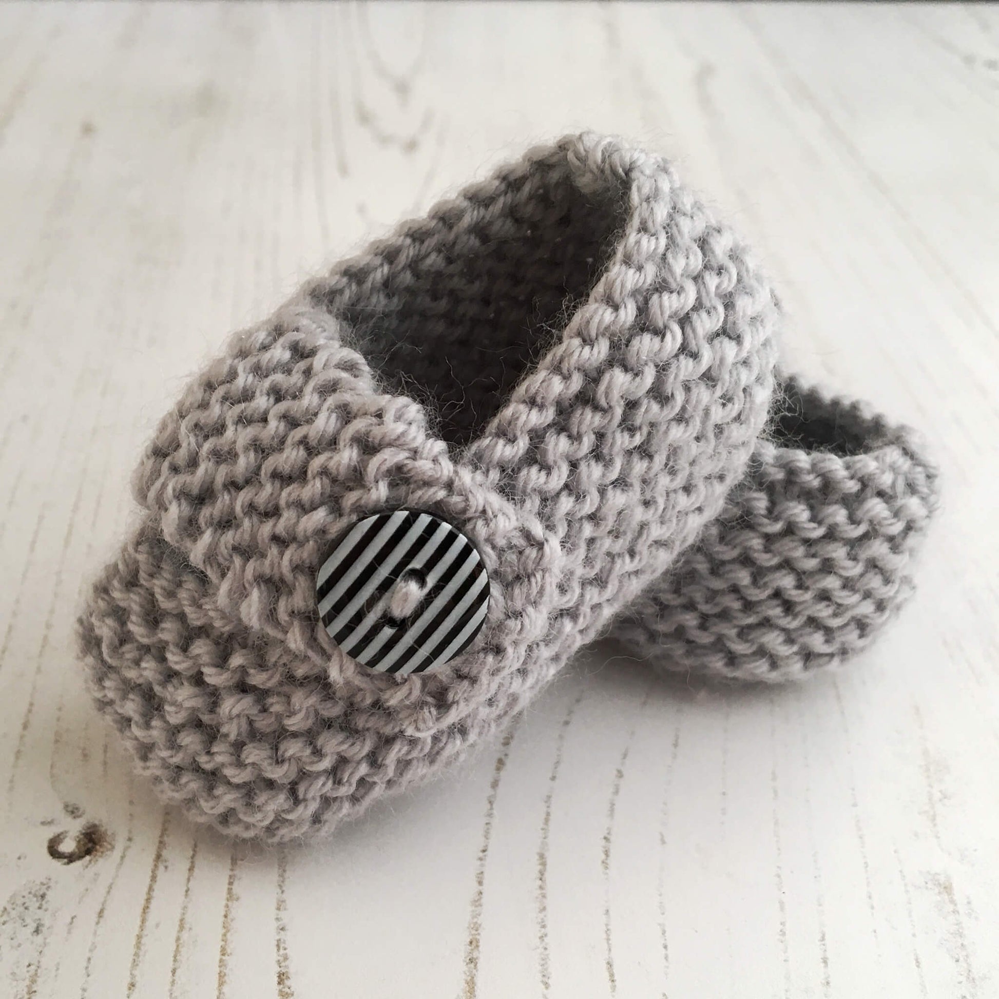 a simple baby shoes knitting pattern. sample is shown in grey yarn with black and white striped buttons