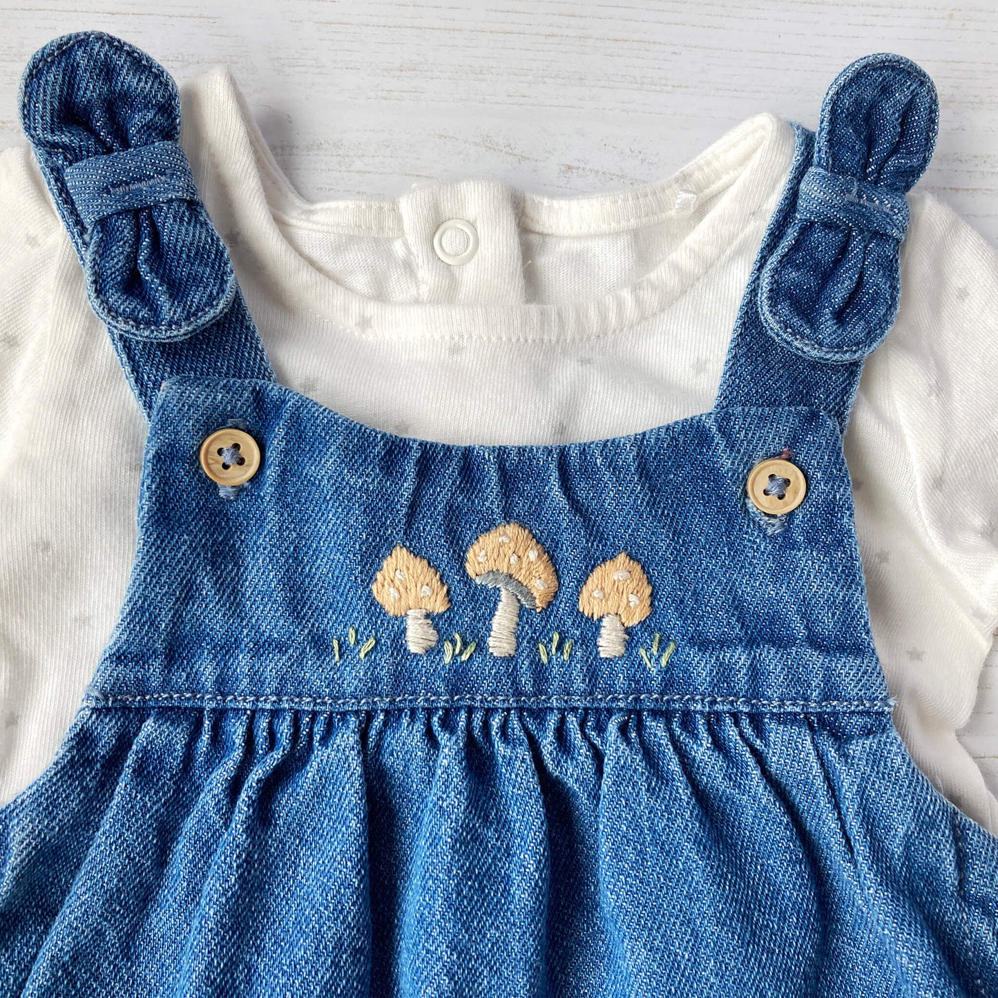 toadstool embroidery pattern for baby clothing. toadstool embroidery is shown on the yoke of a denim pinafore dress