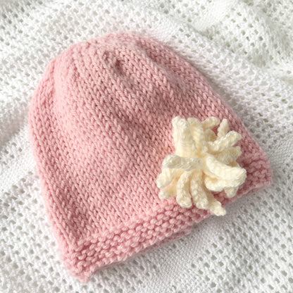 a baby and child hat knitting pattern with flower. shown knitted in pink with cream flower