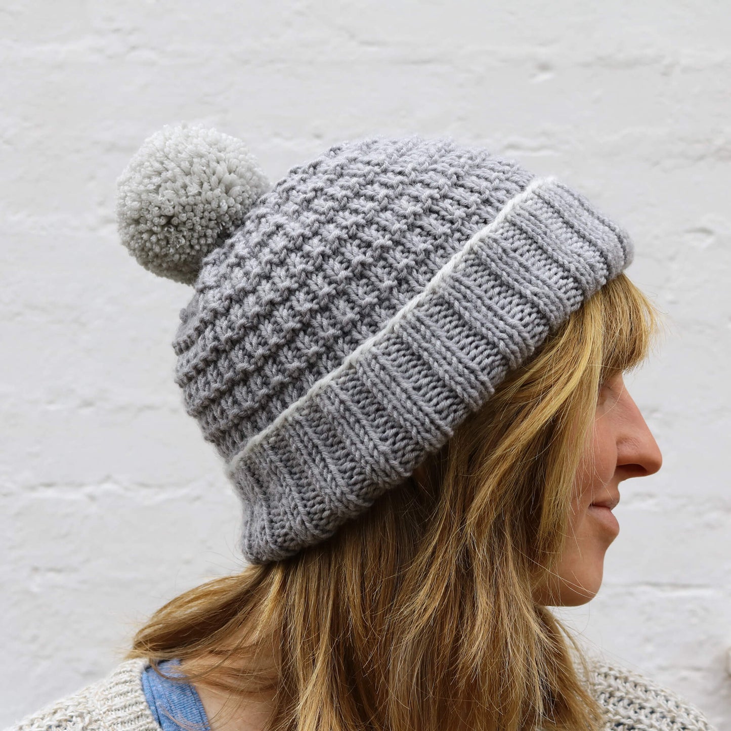 a hat knitting pattern with baby to adult sizes. photo show side view on a model against a white wall