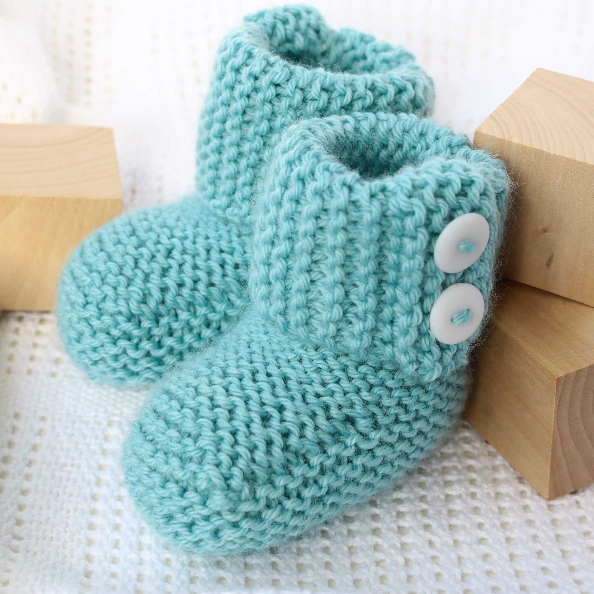 a booties knit pattern. the booties are styled with wooden blocks on a white blanket
