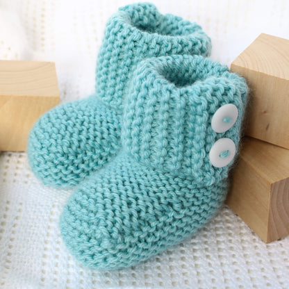 a booties knit pattern. the booties are styled with wooden blocks on a white blanket