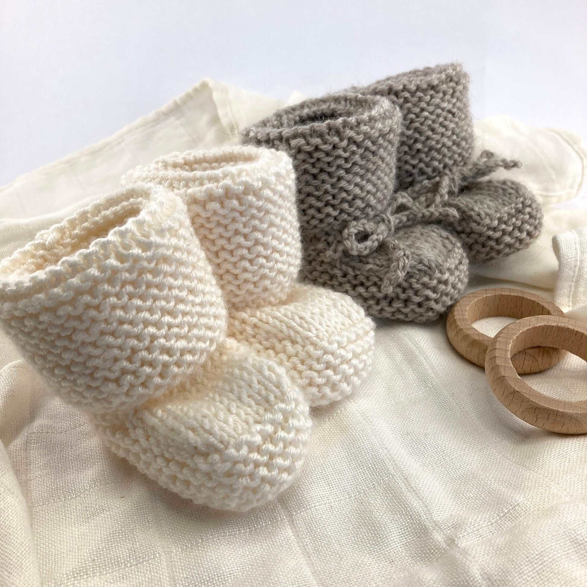 a baby booties pdf knitting pattern for two styles of booties. one is shown in grey with knitted ties, the other in white yarn without ties
