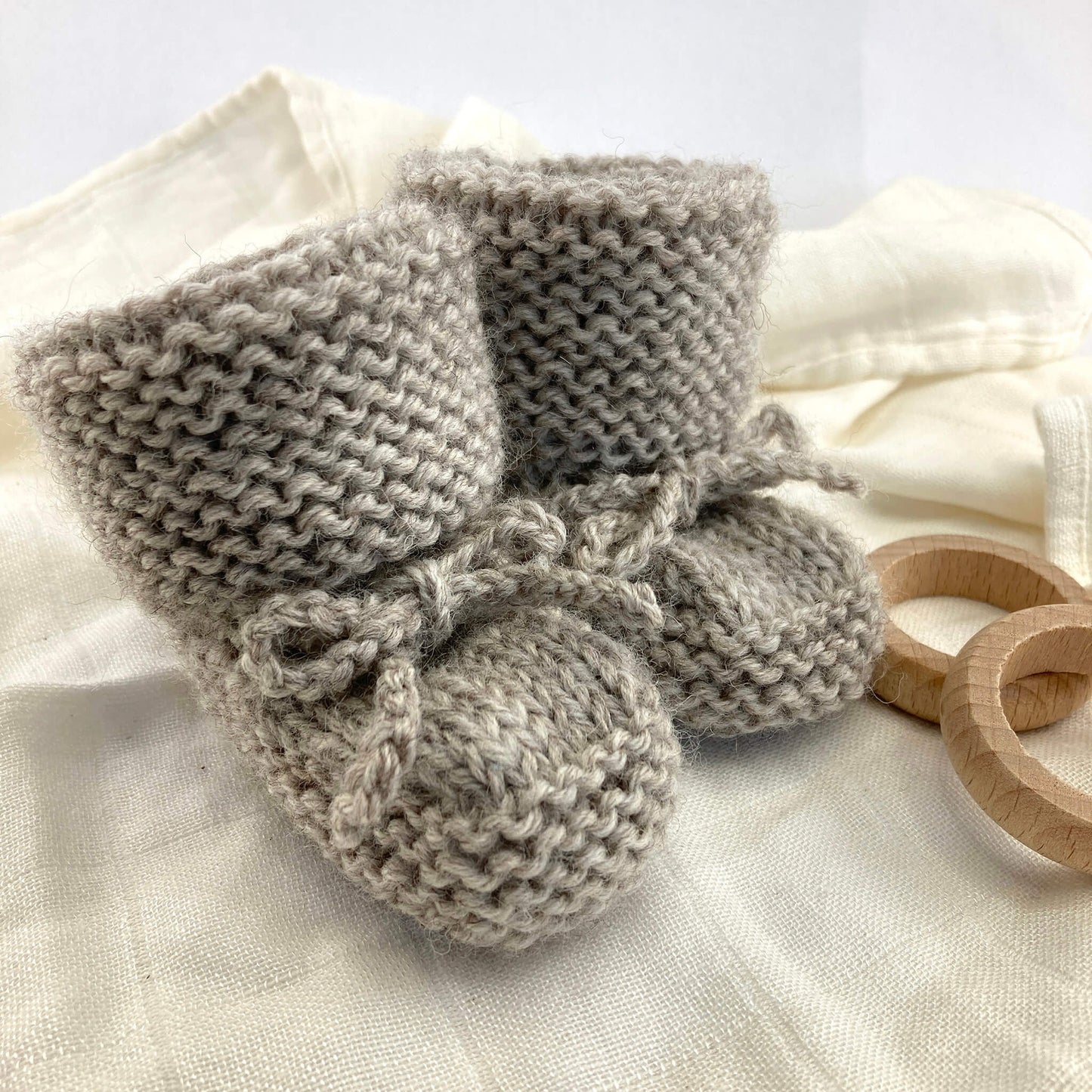 sample for an easy booties knitting pattern kniited in grey yarn and styled on a white muslin