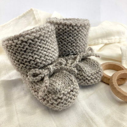 sample for an easy booties knitting pattern kniited in grey yarn and styled on a white muslin