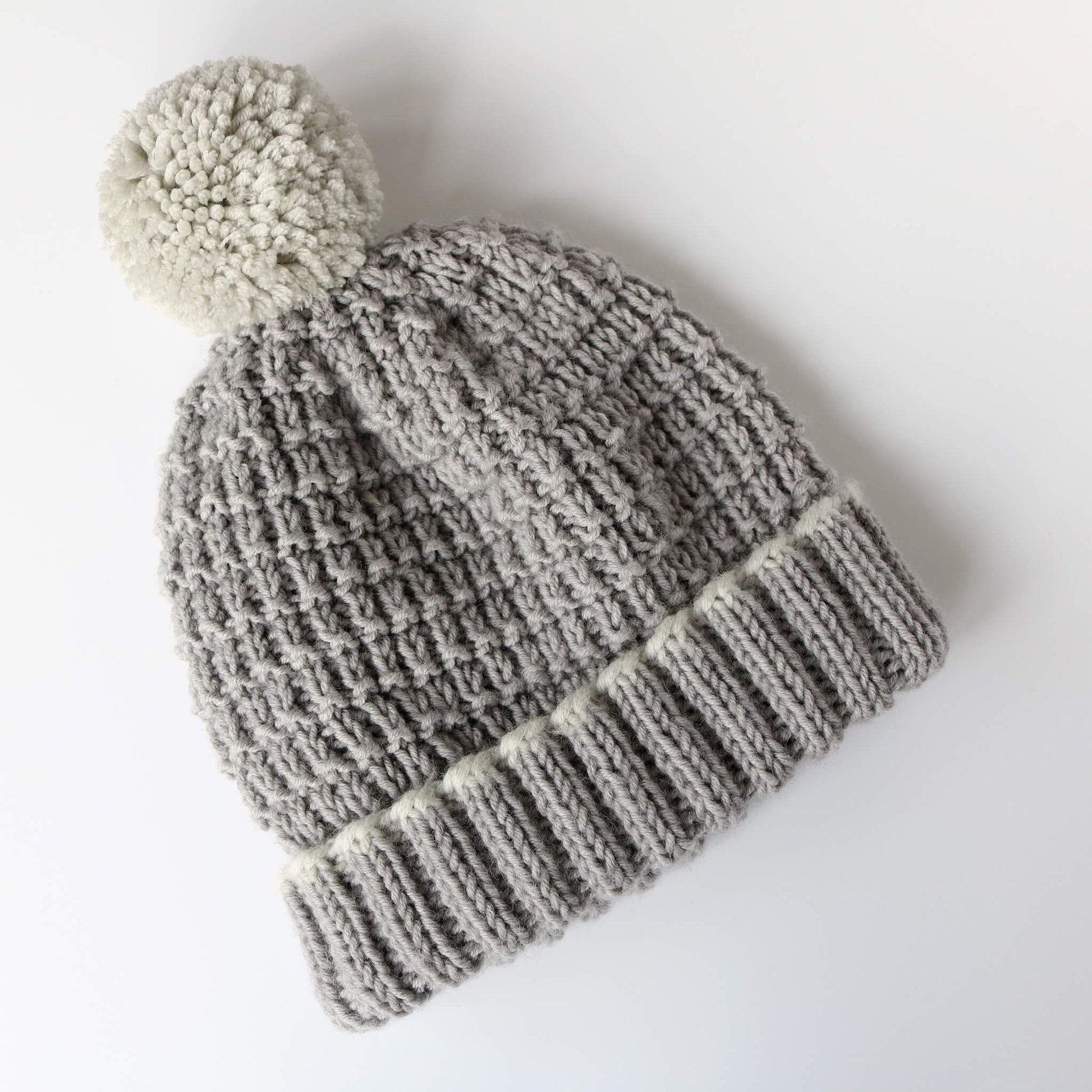 an easy hat knitting pattern shown knit in grey yarn with light grey pompom