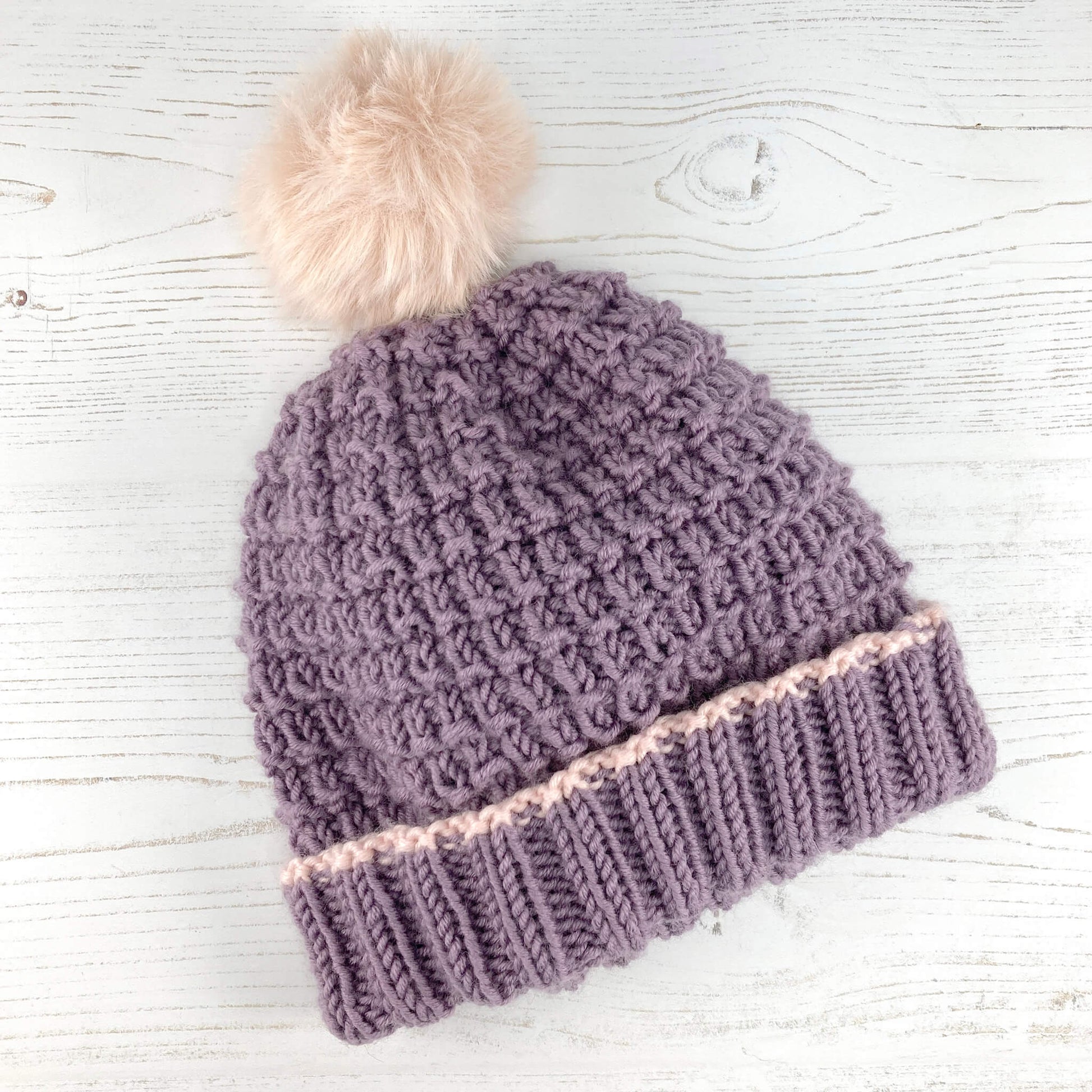 an easy to knit hat pattern shown in lilac colour yarn with a pink pompom