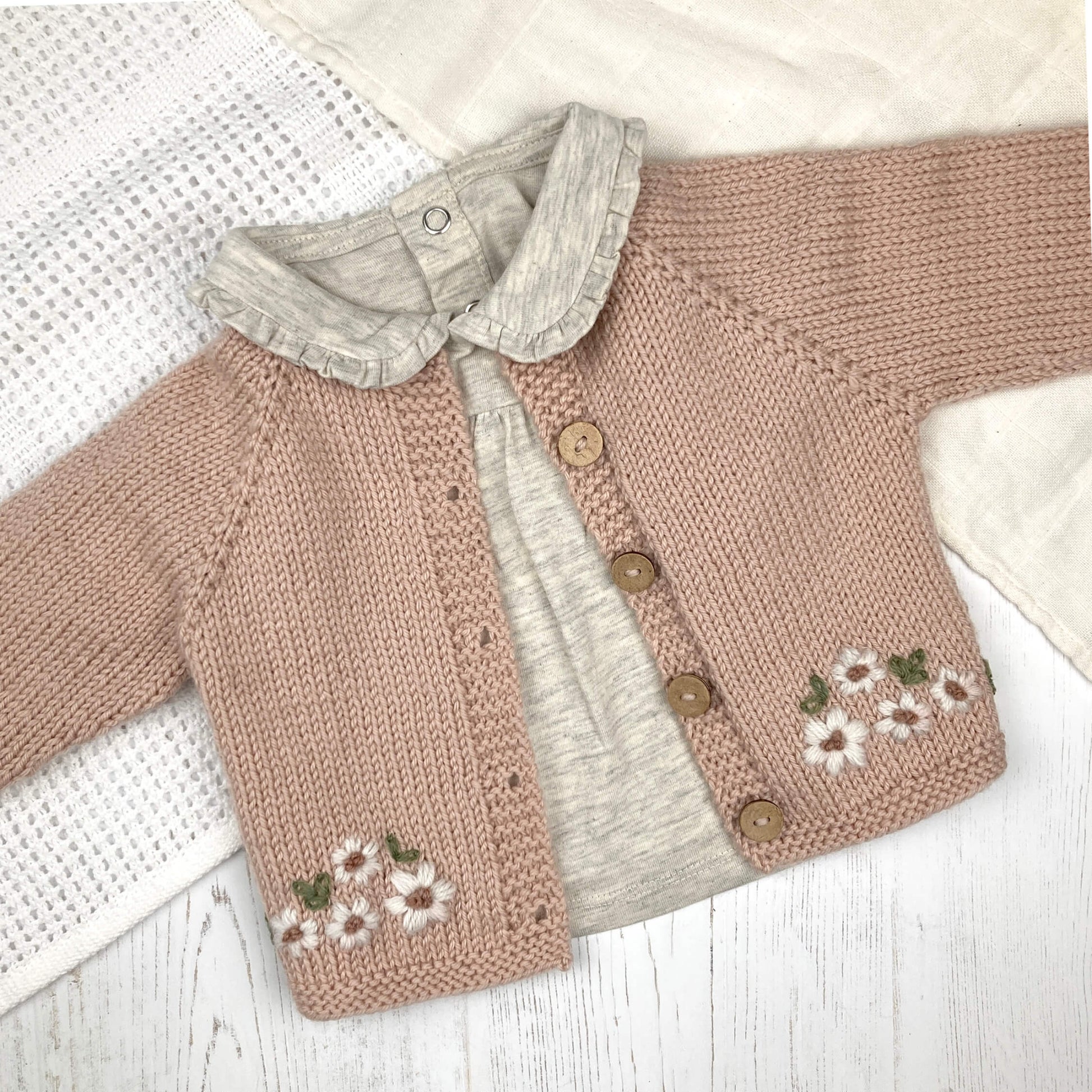 baby cardigan knitting pattern with floral embroidery shown on a white blanket