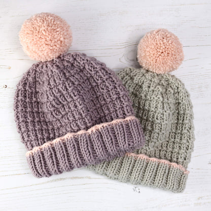 a hat knitting pattern with fold back brim and pompom. samples are in lilac and grey with pale pink pompoms
