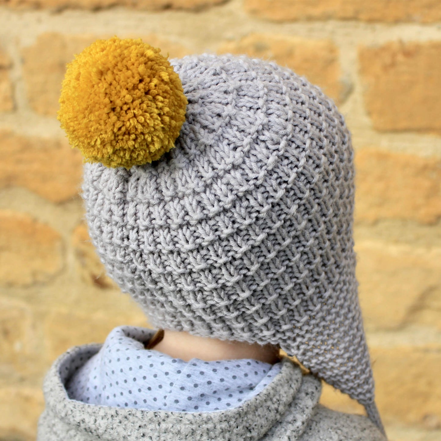 photo shows the rear view of a kids earflap hat with pompom