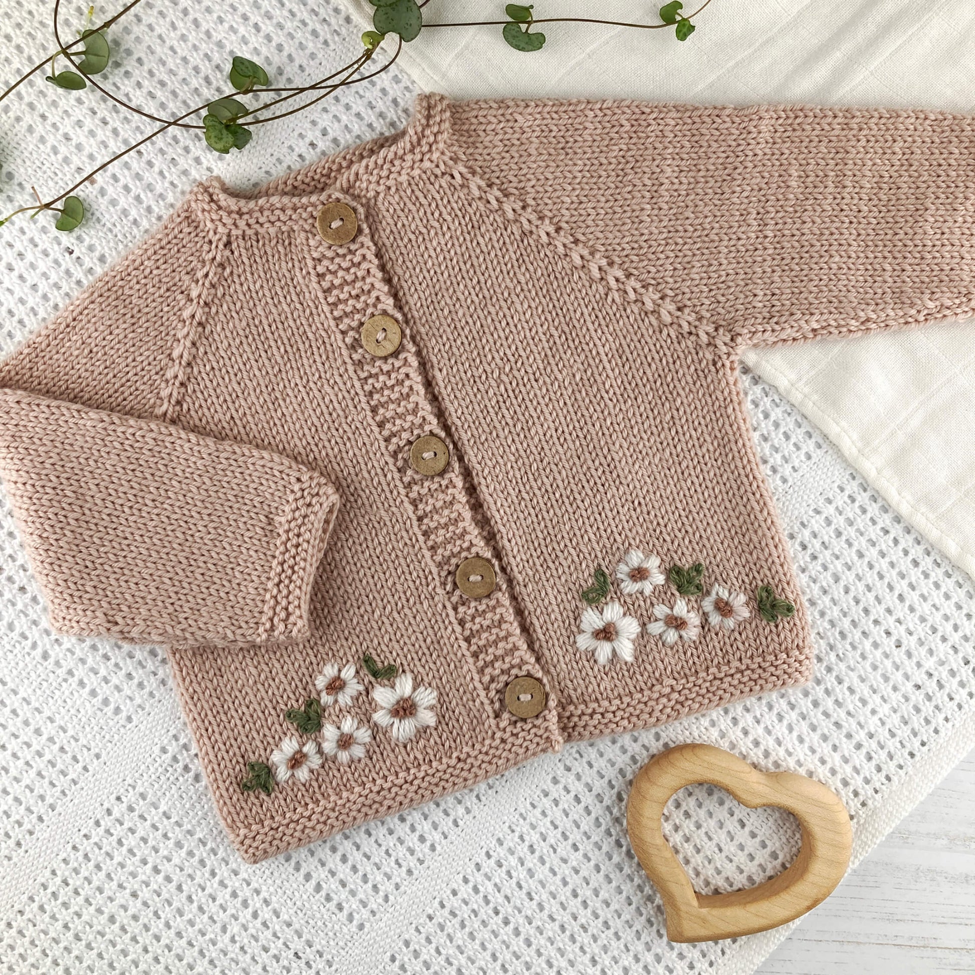 baby cardigan knitting pattern with floral patterns and buttons on a white textured  blanket