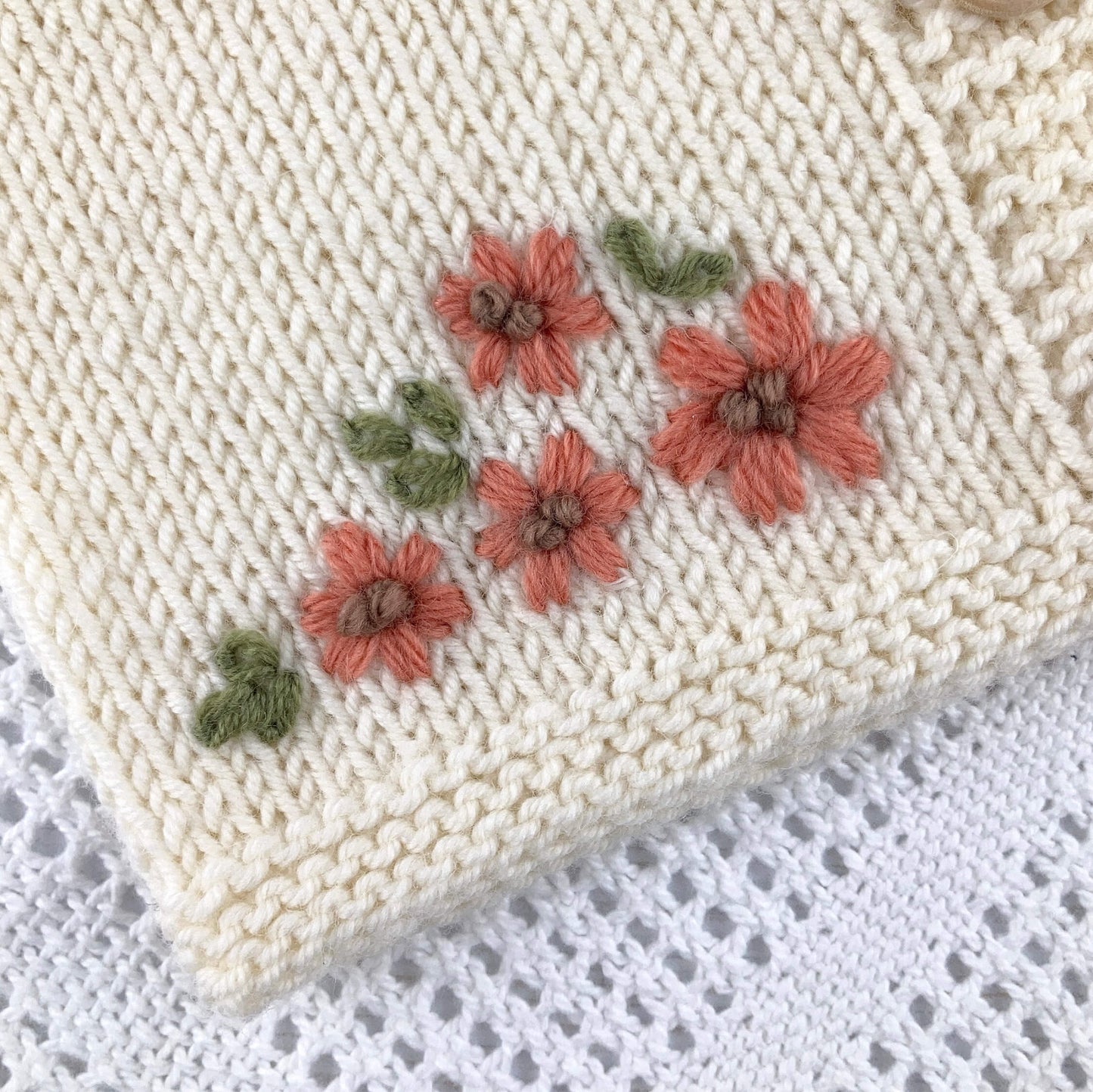 close up view of baby cardigan knitting pattern with embroidered flowers 