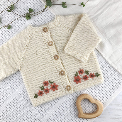 baby cardigan knitting pattern with floral embroidery shown on a white blanket